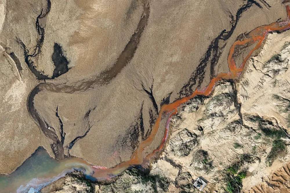 From the air: a dry river bed in Sherpur district, cracked and grey, with a thin orange trickle of water